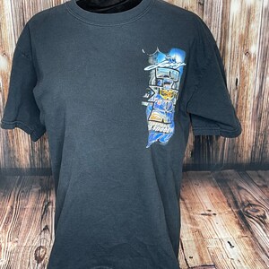 Może przedstawiać: Czarny t-shirt z kr&oacute;tkim rękawem z grafiką na prawej g&oacute;rnej części klatki piersiowej. Nadruk przedstawia kierowcę wyścigowego w niebieskim kasku, z napisem "Larry" powyżej, "Zone" dużymi literami oraz "Experience the speed of life" poniżej.