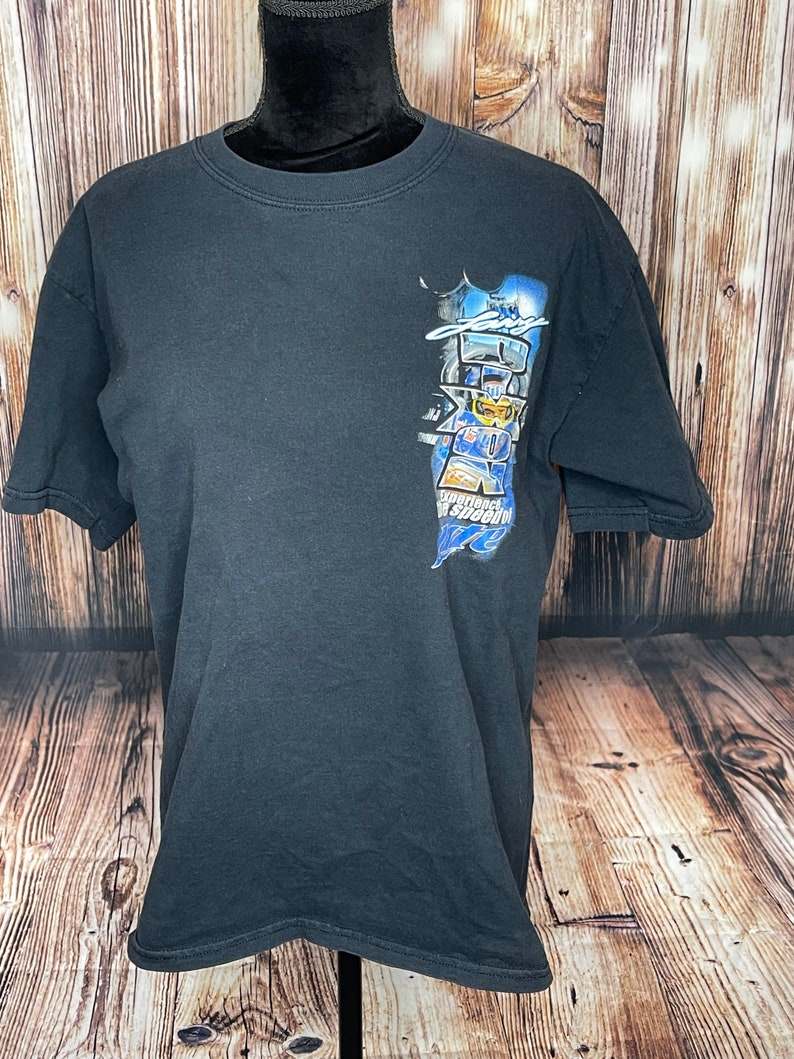 Może przedstawiać: Czarny t-shirt z kr&oacute;tkim rękawem z grafiką na prawej g&oacute;rnej części klatki piersiowej. Nadruk przedstawia kierowcę wyścigowego w niebieskim kasku, z napisem "Larry" powyżej, "Zone" dużymi literami oraz "Experience the speed of life" poniżej.