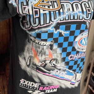 May include: Black t-shirt featuring a drag racing design. The graphic includes a race car with the text "EXIDE Batteries Racing Team" and "Zorie Go Racing". The design incorporates a checkered flag pattern and the words "NHRA Top Fuel Champion".