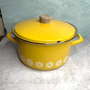 May include: A bright yellow enamel pot with a matching lid and wooden handle. The pot has two side handles and a decorative white pattern around the base. A classic kitchenware item.