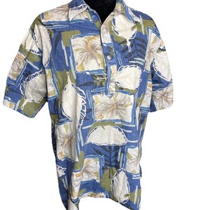 May include: Short-sleeved button-up shirt with a floral pattern. The shirt features a blue background with white, green, and tan floral and leaf designs. The shirt has a collar and a button-down front.