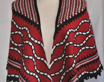 Puede incluir: Un chal de punto rojo, blanco y negro con un patrón geométrico. El chal tiene un borde festoneado y está drapeado sobre un maniquí blanco.