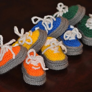 May include: A set of ten crocheted baby shoes in various colors, including blue, green, yellow, and orange. The shoes are all made with a gray crocheted sole.