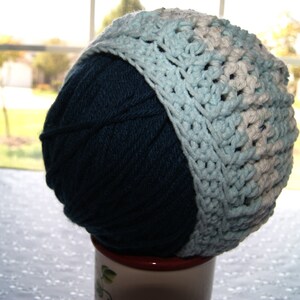May include: A blue and white crocheted hat with a yarn ball inside. The hat is made with a combination of light blue and white yarn.