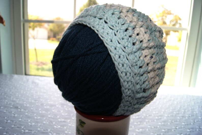 May include: A blue and white crocheted hat with a yarn ball inside. The hat is made with a combination of light blue and white yarn.