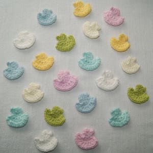 Puede incluir: Una colección de 19 adornos de pato de ganchillo en varios colores pastel, incluyendo rosa, azul, amarillo y verde. Los patos son todos de aproximadamente el mismo tamaño y están dispuestos en un patrón aleatorio.