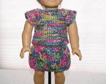 May include: A colorful crochet doll outfit, featuring a top and skirt. The top has short sleeves and the skirt is a matching design. The yarn is a mix of pink, blue, green, and yellow. The outfit is designed for a doll.