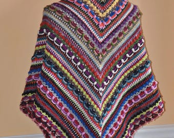 Puede incluir: Un chal de ganchillo hecho a mano y colorido, exhibido en un maniquí. El chal presenta una variedad de colores, incluyendo rojo, morado, azul y amarillo, dispuestos en rayas y patrones decorativos. El chal triangular tiene un borde festoneado.