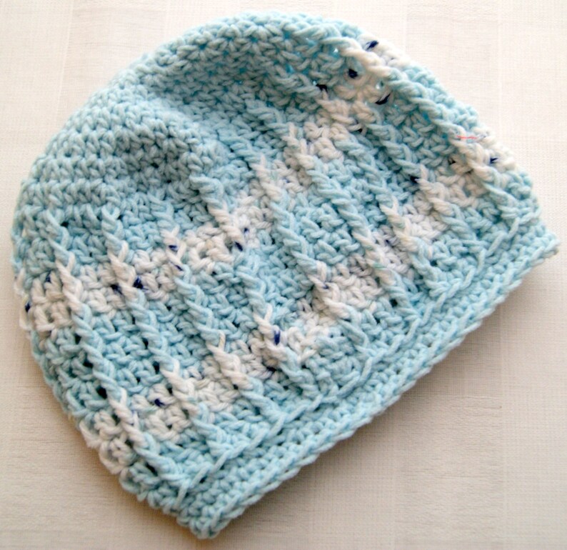 May include: A blue and white crocheted beanie hat. The hat is made with a textured stitch and has a striped pattern.