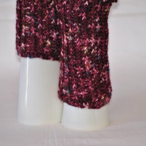 May include: Close-up of a knitted leg warmer in a deep burgundy color with flecks of other colors. The leg warmer is displayed on a white cylindrical form. The knit pattern is visible.
