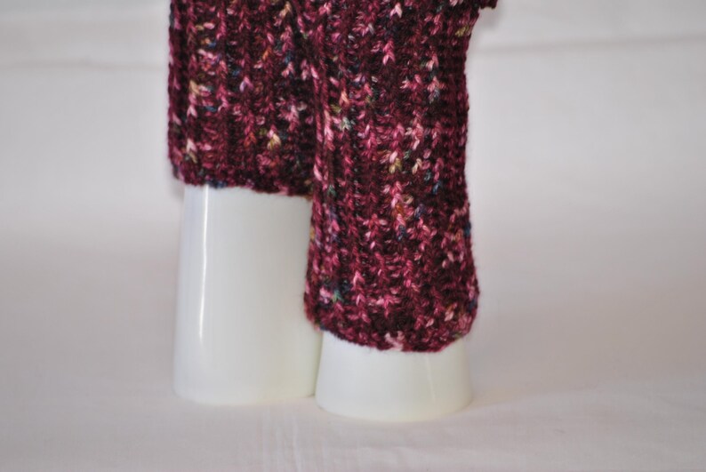May include: Close-up of a knitted leg warmer in a deep burgundy color with flecks of other colors. The leg warmer is displayed on a white cylindrical form. The knit pattern is visible.