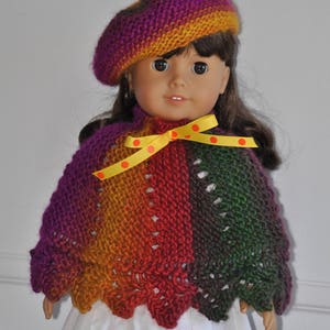 May include: A doll wearing a multi-colored knitted poncho with a yellow ribbon and polka dots, and a purple and orange knitted beret.