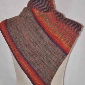 Puede incluir: Una bufanda de punto triangular con un patr&oacute;n de chevron en tonos de marr&oacute;n, naranja y morado.