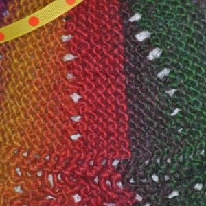May include: Close-up of a knitted fabric with a gradient of purple, orange, red, and green. The fabric has a textured, woven appearance.