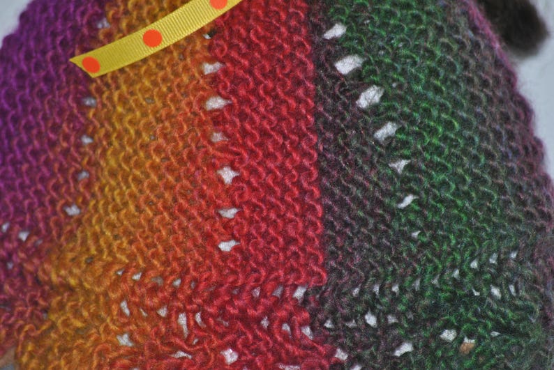 May include: Close-up of a knitted fabric with a gradient of purple, orange, red, and green. The fabric has a textured, woven appearance.