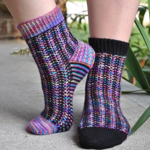 May include: A pair of colorful socks with a black background and a black cuff. The socks have a striped pattern with pink, blue, green, and yellow stripes.