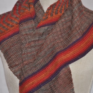 Puede incluir: Una bufanda de punto marr&oacute;n y gris con un patr&oacute;n de rayas multicolores en tonos naranja, rojo y morado.