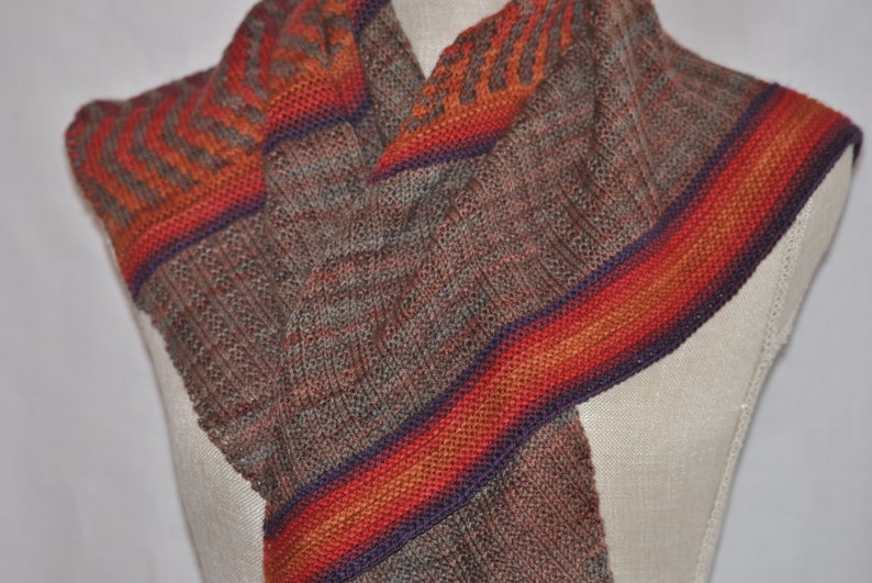 Puede incluir: Una bufanda de punto marr&oacute;n y gris con un patr&oacute;n de rayas multicolores en tonos naranja, rojo y morado.