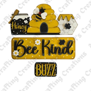 May include: A set of wooden decorative cutouts featuring a black honey jar with a dipper, a yellow beehive with a bee, a hexagonal honeycomb piece, a yellow rectangular sign with the text Bee Kind, and a small black sign with the text BUZZ.
