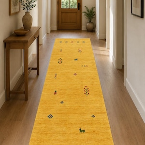 Puede incluir: Una alfombra de pasillo larga y rectangular en un tono amarillo mostaza vibrante. La superficie presenta pequeños motivos bordados dispersos en rojo, azul y verde, incluyendo diminutas formas florales, diamantes geométricos y figuras animales.