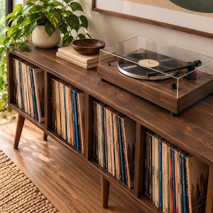 May include: A dark wood media console with four open storage compartments filled with vinyl records. A turntable with a clear acrylic dust cover sits on the top surface, alongside a small wooden bowl and two stacked books.