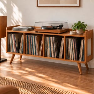 Könnte beinhalten: Ein Medienmöbel aus Holz mit vier offenen Fächern, die mit Schallplatten gefüllt sind. Ein Plattenspieler mit transparenter Abdeckung steht obenauf. Zwei hohe Lautsprecherständer aus Holz mit schwarzen Sockeln flankieren das Möbelstück.