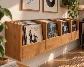 Puede incluir: Una unidad de almacenamiento de vinilos de madera marrón claro montada en la pared con cuatro compartimentos abiertos. Los estantes están llenos de varios álbumes de vinilo, incluidos Fleetwood Mac Rumours, The Beatles Abbey Road, Daft Punk y Amy Winehouse.