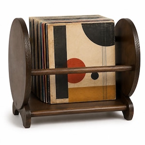 May include: A dark brown wooden record holder featuring two circular side panels and a horizontal support bar. The rack contains a collection of vinyl records, with the front cover displaying a geometric design of black, red, and tan shapes.