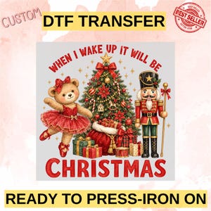 May include: A custom DTF transfer featuring a teddy bear in a red tutu, a decorated Christmas tree, and a nutcracker soldier. The text reads "WHEN I WAKE UP IT WILL BE CHRISTMAS". The design includes wrapped gifts and a red sack at the base.