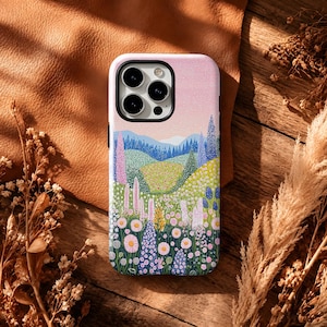 May include: A smartphone case featuring a colourful illustration of a rolling landscape with a pink sky, green hills, blue mountains, and a foreground filled with various pink, purple, and white wildflowers and tall green grasses.