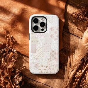 May include: A white smartphone case featuring a patchwork design of various soft pink and cream floral patterns, small dots, and tiny teddy bear motifs. The case has a black camera cutout frame and covers the back of the mobile device.