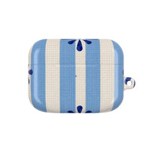 Puede incluir: Una funda protectora rectangular para auriculares inalámbricos con un patrón de cuadrícula y rayas verticales alternas en azul claro y crema. El diseño incluye detalles florales en azul oscuro y una pequeña abertura circular en el lado derecho.
