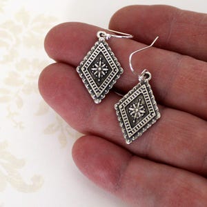 May include: A pair of silver dangle earrings with a diamond-shaped design. Each earring features a small, intricate star-shaped design in the center.