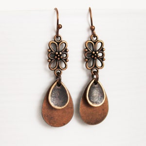 May include: A pair of copper-toned dangle earrings with a floral design and two teardrop-shaped charms.