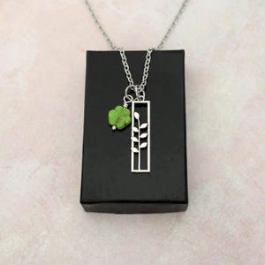 May include: A silver necklace with a green stone charm and a silver pendant shaped like a branch with leaves.