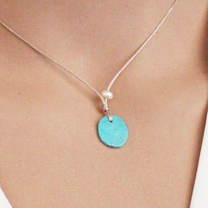 May include: A turquoise oval pendant necklace with a white pearl accent on a thin beige cord.