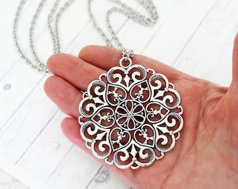 May include: A silver filigree pendant necklace with a large, intricate, circular design. The pendant features a repeating pattern of swirls and hearts.