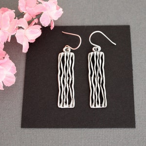 May include: A pair of silver earrings with a textured, wavy design. The earrings are hanging from a black background.