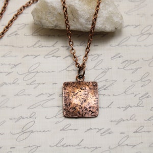 May include: A copper necklace with a square pendant. The pendant has a hammered texture and a rustic finish.