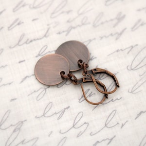 May include: A pair of copper earrings with a simple round disc design. The earrings have a hook closure.