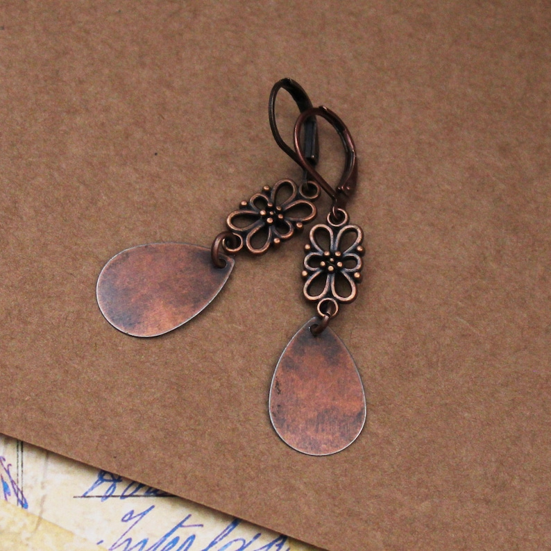 May include: Copper teardrop earrings with a floral design. The earrings are a light copper color and have a distressed finish.