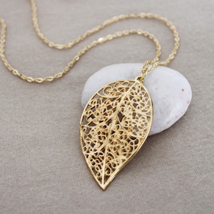 May include: A gold leaf pendant necklace with a delicate filigree design. The pendant is shaped like a leaf and has a detailed, intricate pattern.
