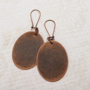 May include: A pair of oval-shaped earrings with a rustic copper finish. The earrings are made of metal and have a simple design.
