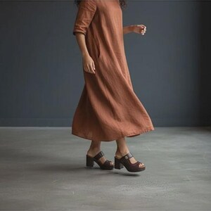 May include: A rust-colored midi-length dress with short sleeves and a loose, flowing silhouette, paired with dark brown platform sandals featuring a thick strap and a block heel. The dress reaches below the knees and has a simple, unadorned design.
