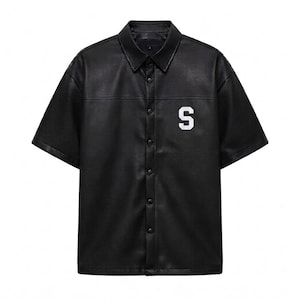 May include: A black short-sleeved shirt made of a smooth, leather-like material. It features a classic collar, a front button-down placket with snap closures, and a white letter S patch on the upper left chest area. The shirt has a straight hem.