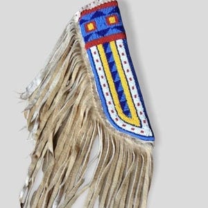 May include: A tan leather accessory featuring a long fringe and a rectangular panel decorated with intricate beadwork. The beadwork displays a geometric pattern in vibrant shades of blue, yellow, red, and white, arranged in vertical stripes.