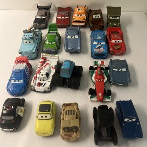 May include: A collection of nineteen die-cast toy cars featuring various colors, shapes, and character designs. The assortment includes race cars, trucks, and vintage vehicles, each with painted details, windshield eyes, and unique body styles.