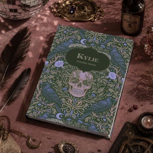 Pu&ograve; includere: Un taccuino rettangolare con copertina verde scuro caratterizzato da un motivo ripetuto di corvi neri, fiori viola chiaro e un teschio umano centrale. Un'etichetta verde scuro al centro riporta il testo KYLIE e October Notes in bianco.