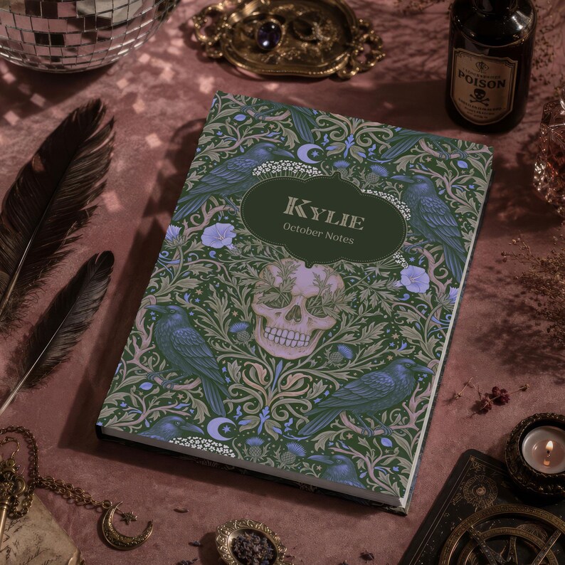 Pu&ograve; includere: Un taccuino rettangolare con copertina verde scuro caratterizzato da un motivo ripetuto di corvi neri, fiori viola chiaro e un teschio umano centrale. Un'etichetta verde scuro al centro riporta il testo KYLIE e October Notes in bianco.