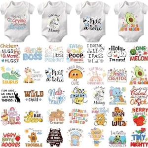 May include: A collection of white short-sleeved baby bodysuits featuring various colourful graphic prints and text designs, including phrases like I'm Not Crying I'm Ordering Dinner, Milk-a-holic, Let's Just Avocuddle, Tiny Boss, and Little Peanut.